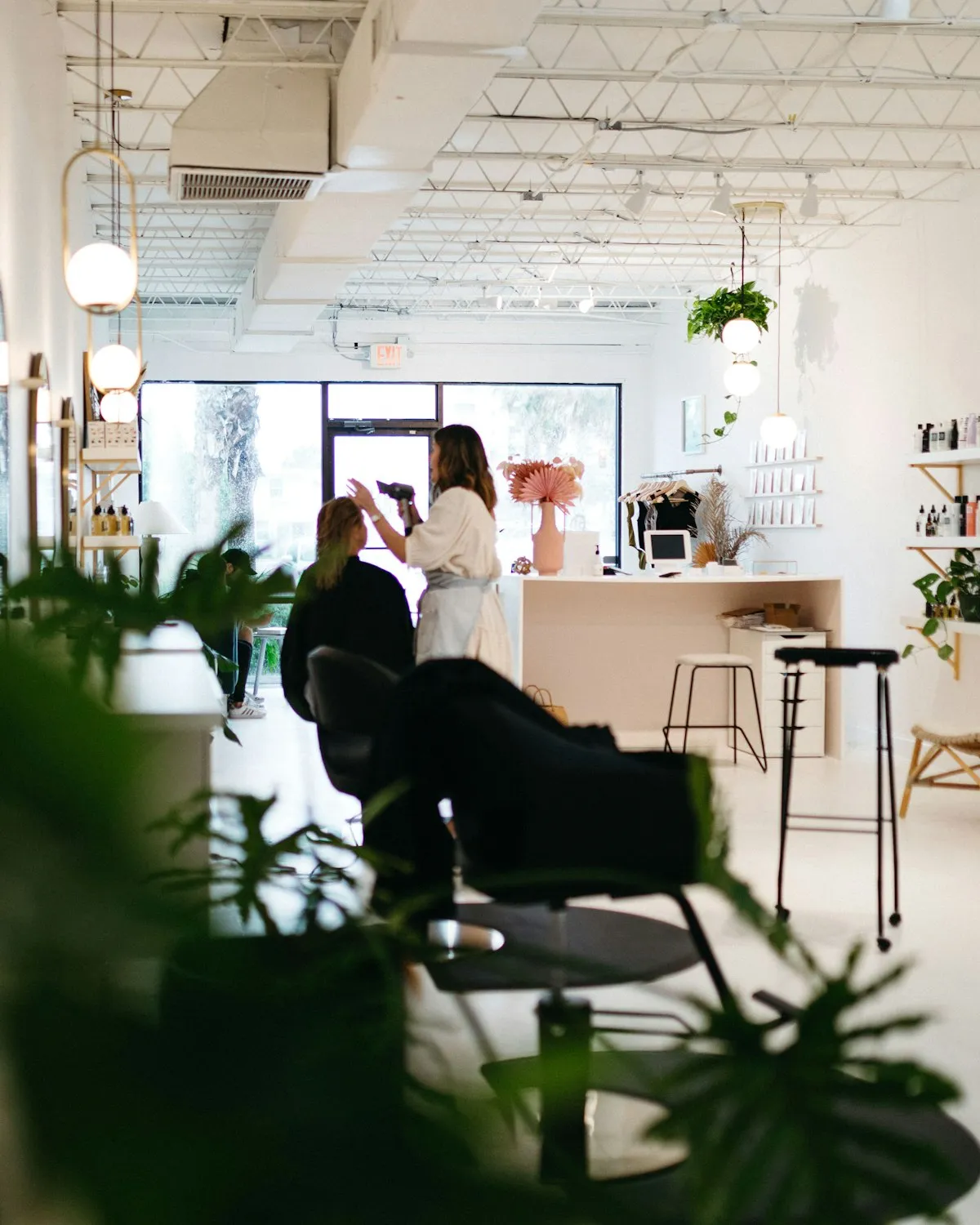 Interior de salon văzut printre plante verzi: scaune de coafor, recepție și lumină naturală