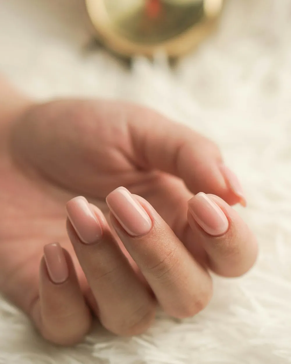 Mână cu unghii ovale, semipermanentă nude-piersică, pe o blană albă